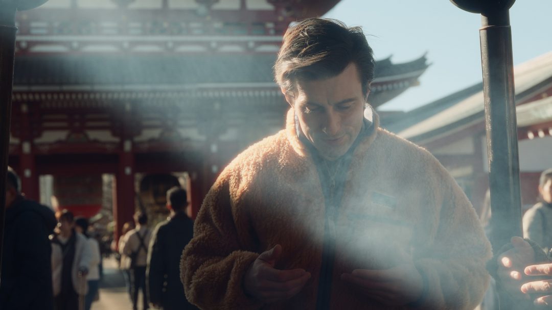 Man at temple surrounded by incense smoke, smiling in sunlight.