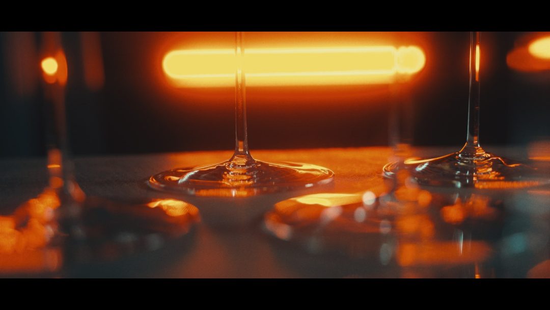 Close-up of wine glass bases on reflective bar surface with warm lights.