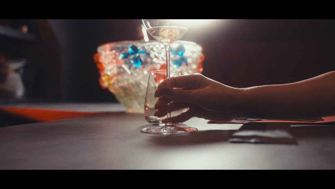 Hand holding champagne glass on bar beside ice bucket.