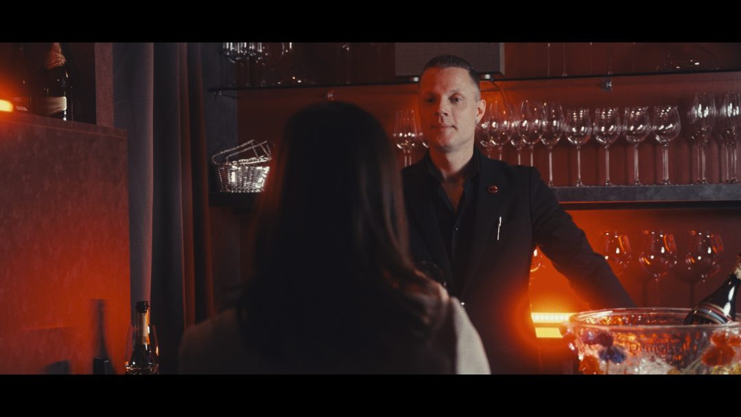 Bartender speaking with guest across bar counter, bottles behind.
