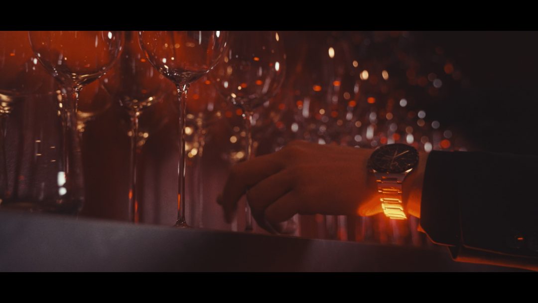 Hand reaching for wine glass among rows of glassware, warm reflections.