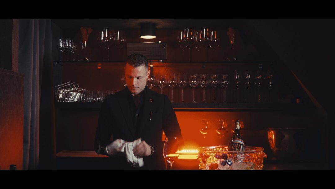 Bartender polishing glass behind bar with shelves of wine glasses.