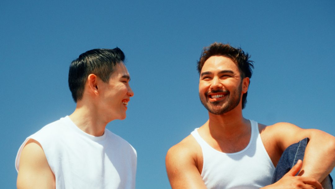 Two men smiling and looking at each other against blue sky.