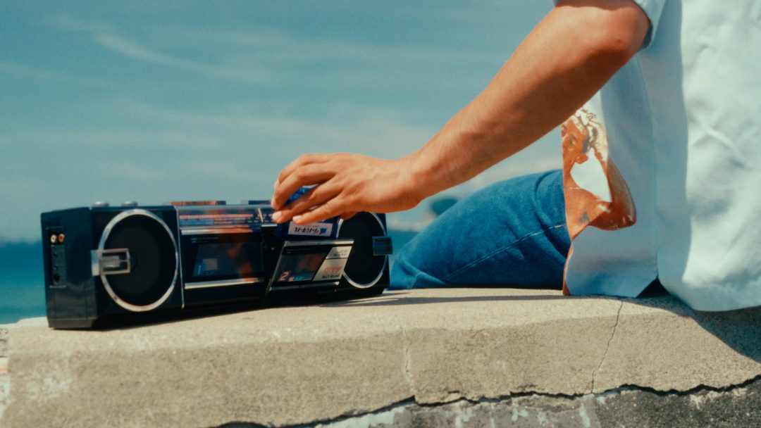 Lower body of man inserting blue cassette on stone ledge by sea.