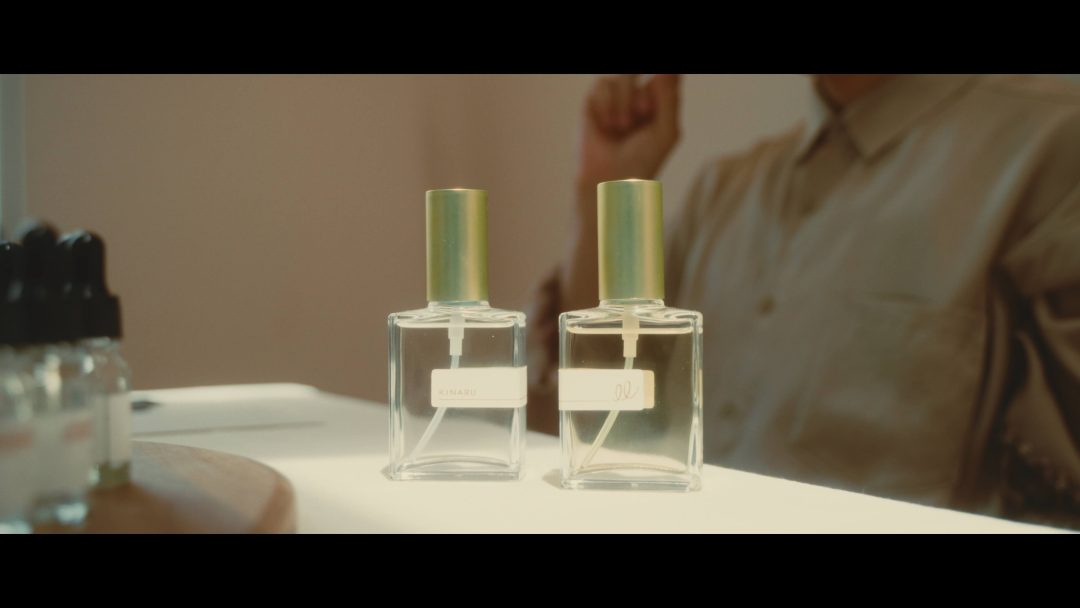 Two perfume bottles on table with blurred figure behind.