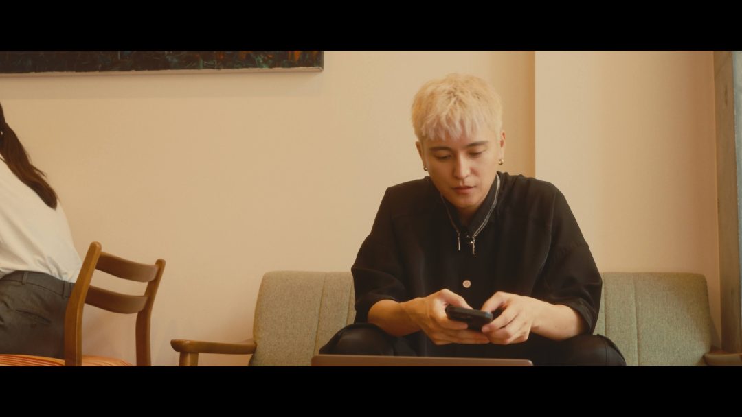 Man with blond hair sitting indoors using phone.