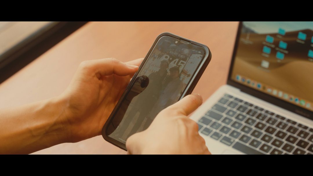Close-up of hands holding smartphone, laptop on desk.