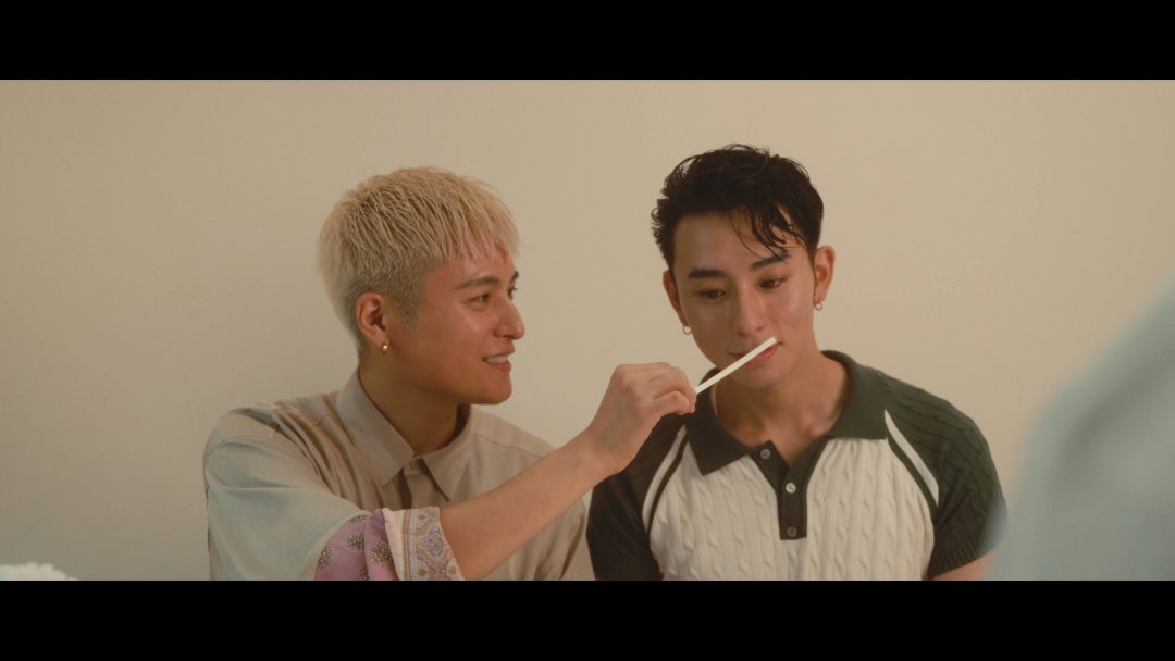 Man smiling while letting another man smell perfume test strip.