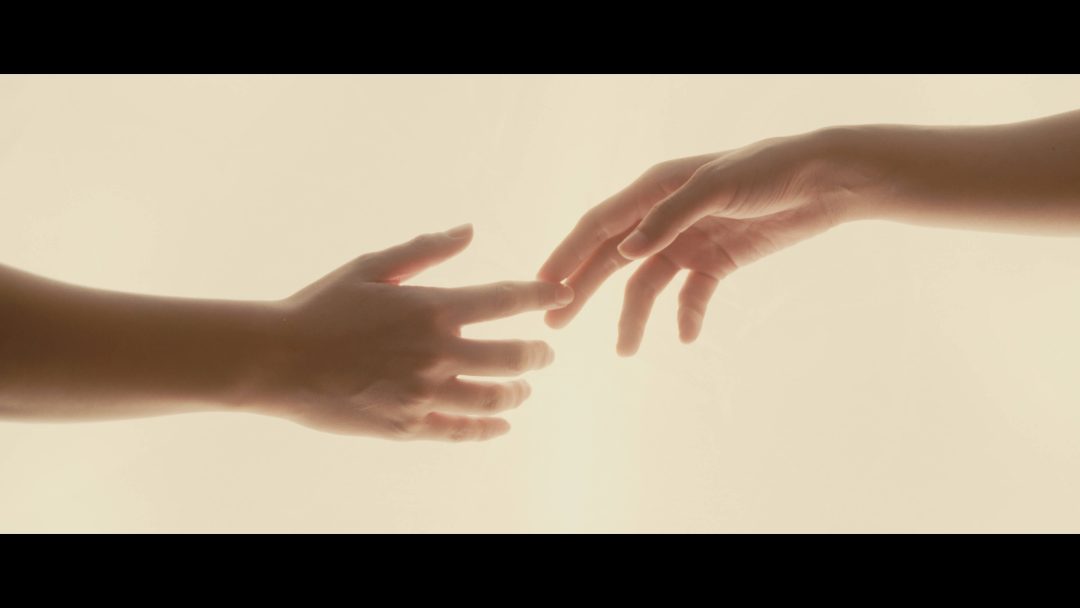 Two hands reaching toward each other against bright background.