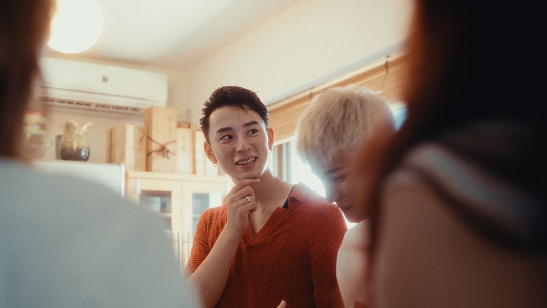 Man in red shirt in kitchen, foreground figures out of focus.