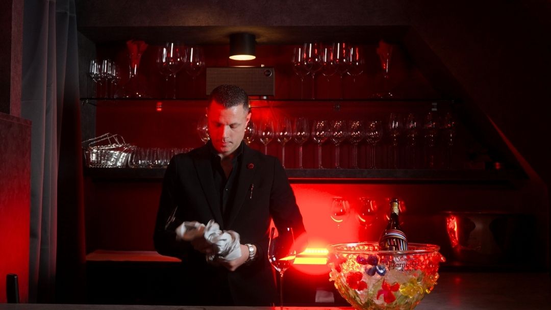 Bar owner cleaning wine glass behind counter with champagne bottle on ice.