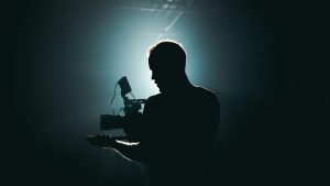 one filmmaker male lit by a backlight white light in the background, he is holding a camera