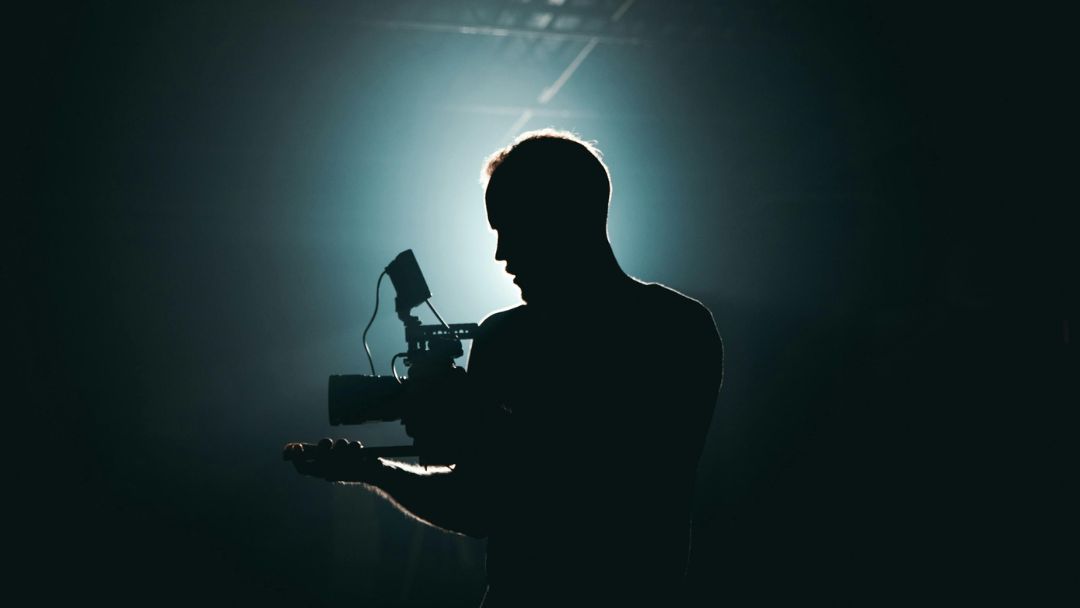 one filmmaker male lit by a backlight white light in the background, he is holding a camera
